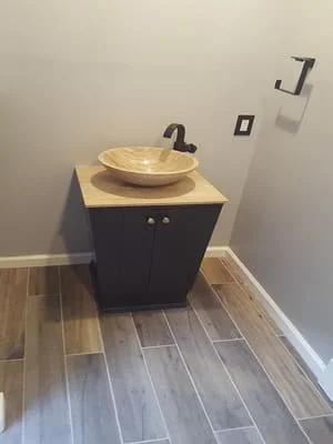 Black vanity cabinet with stone vessel sink and plank tile flooring in powder room