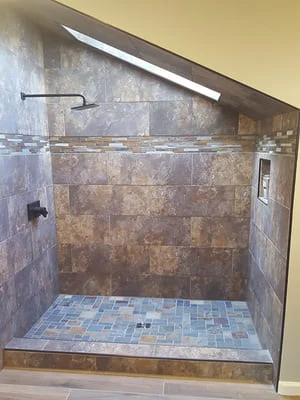 Walk-in shower with tumbled stone tile walls and blue mosaic tile floor, frameless glass enclosure