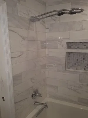 Marble tile shower with glass enclosure, rainfall showerhead, and built-in niche